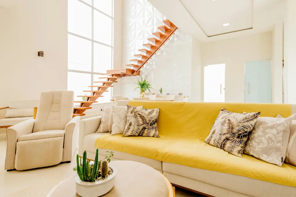 Modern residential interior with yellow sofa, wooden staircase, and bright open layout