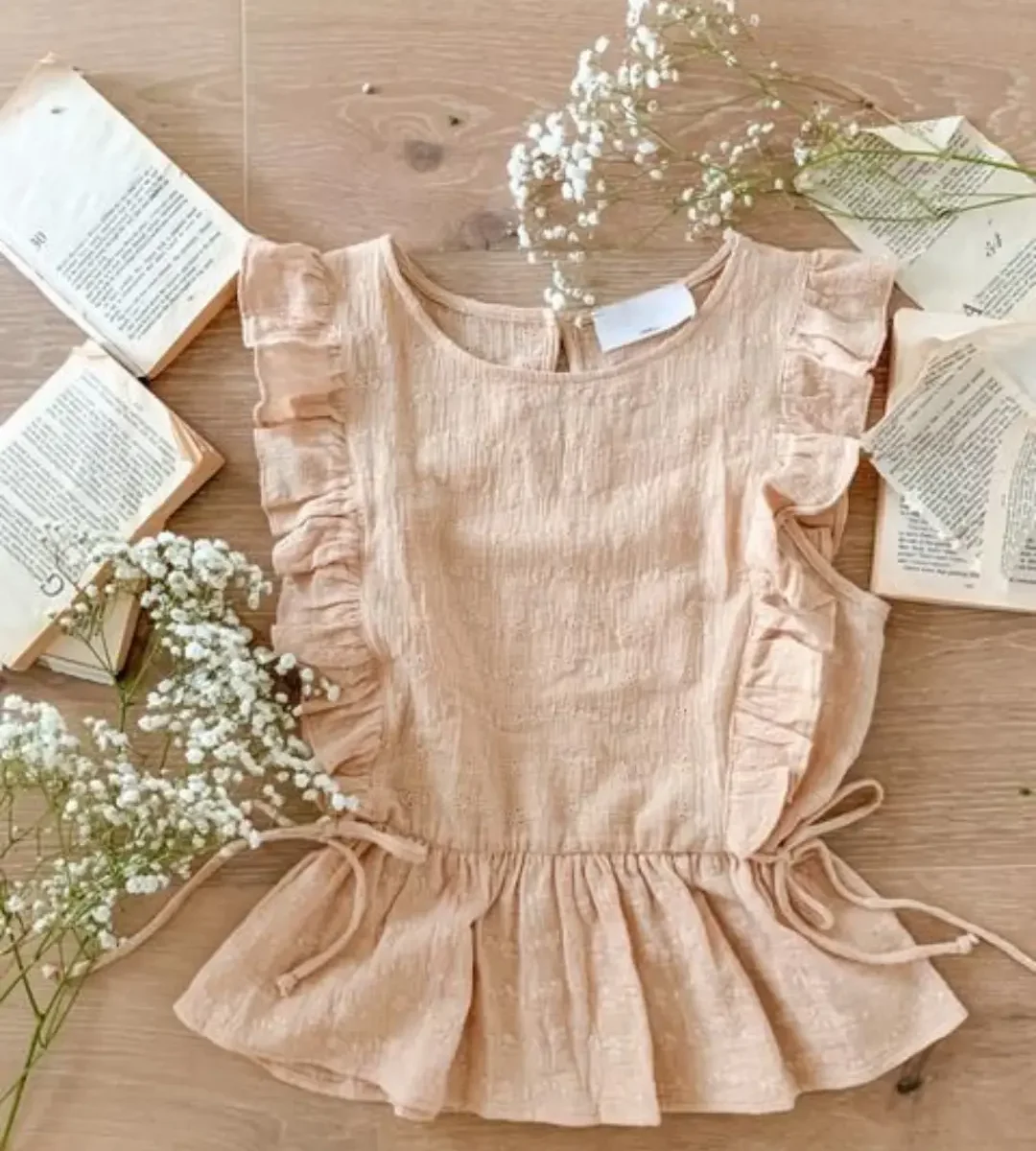 Peach ruffle-sleeve peplum top laid flat with flowers and open books