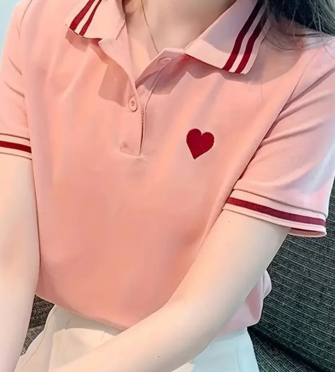 Pink polo shirt with red heart embroidery worn by a woman